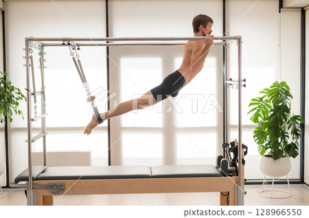 A man performs aerial exercises on a reformer machine. 128966550