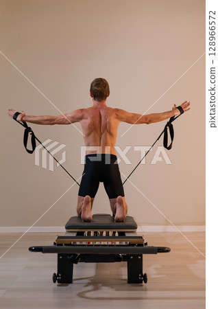 A man doing Pilates on a reformer. A man doing Pilates on a reformer. 128966572