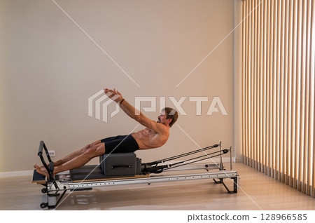 A man doing Pilates on a reformer.  128966585