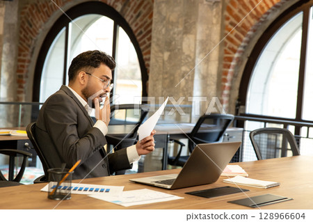 Young businessman scrutinizing document and looking concentrated 128966604