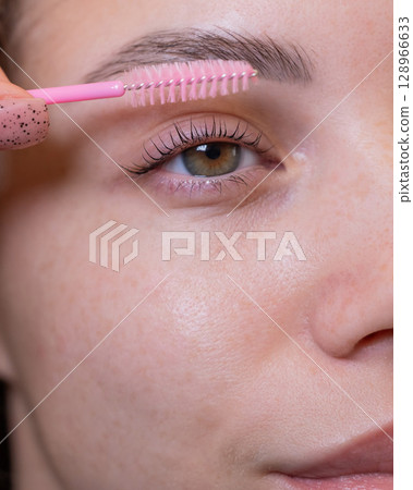 Caucasian woman brushing her eyelashes after lamination. Caucasian woman brushing her eyelashes after lamination. 128966633