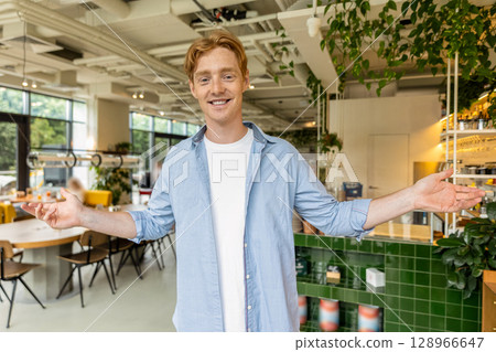 Ginger young guy in blue tshirt welcoming clients in a cafe 128966647