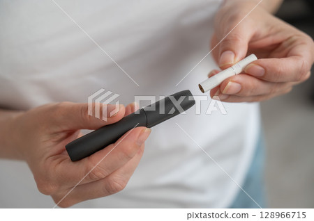 A woman inserts a cigarette stick into a tobacco heating system. Electronic cigarette. A woman inserts a cigarette stick into a tobacco heating system. Electronic cigarette. 128966715