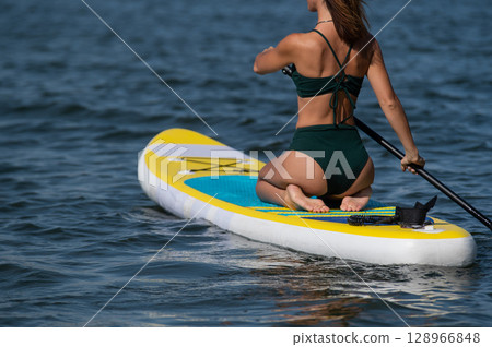 Caucasian woman riding a SUP board on the lake. Summer sport. Caucasian woman riding a SUP board on the lake. Summer sport. 128966848