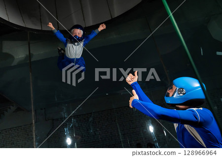 A man teaches a boy to fly in a wind tunnel. Lack of gravity. 128966964