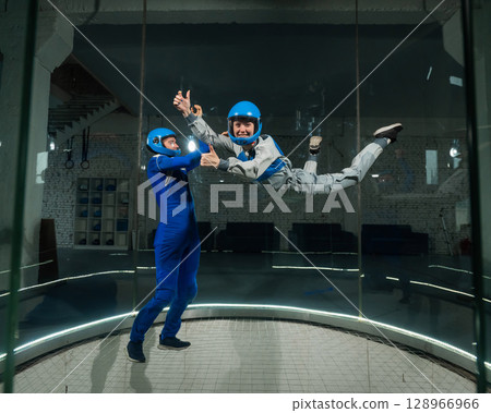 A male instructor teaches a woman how to fly in a wind tunnel. Free fall simulator. 128966966