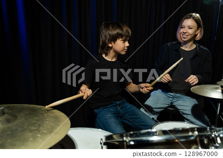 Young caucasian woman teaches a boy to play the drums in the studio on a black background. Music school student 128967000