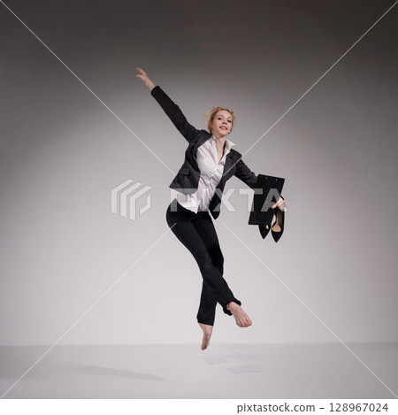 Barefoot ballerina in business suit jumping with laptop on white background. Barefoot ballerina in business suit jumping with laptop on white background. 128967024