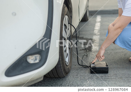 A woman pumps up a tire on a car. A woman pumps up a tire on a car. 128967084