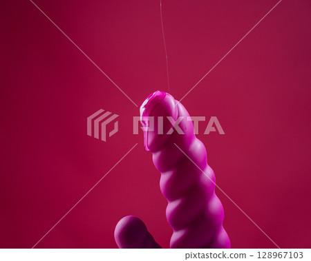 Lube pouring on pink dildo on pink background. Lube pouring on pink dildo on pink background. 128967103