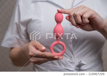 Woman in doctor's coat holding anal beads.  128967299