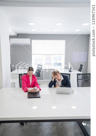 Caucasian Businesswoman Uses Smartphone While Colleague Has Problems At Work.  128967301