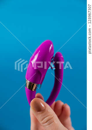 A woman holds a curved sex toy in lubrication on a blue background. Vaginally clitoral vibrator.  128967307