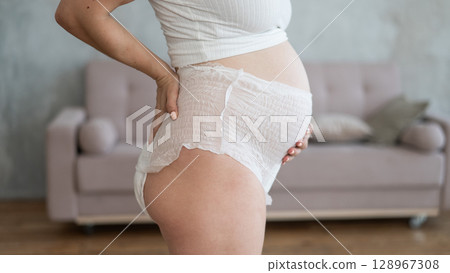 Caucasian pregnant woman in adult diapers suffers from incontinence. Close-up of belly.  128967308