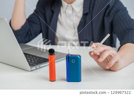 A woman demonstrates different types of cigarettes. An e-cigarette, a disposable vape, and a regular cigarette.  128967322