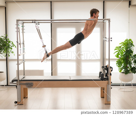 A man performs aerial exercises on a reformer machine. 128967389