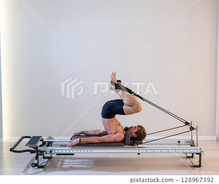 A man doing Pilates on a reformer. A man doing Pilates on a reformer. 128967392
