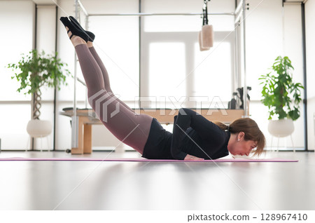 Concentrated woman doing pilates in studio alone. Concentrated woman doing pilates in studio alone. 128967410