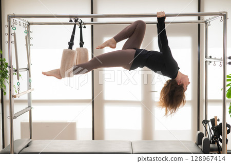 Caucasian woman doing aerial exercises on a reformer machine.  128967414