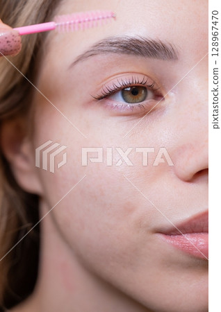 Caucasian woman brushing her eyelashes after lamination. Caucasian woman brushing her eyelashes after lamination. 128967470