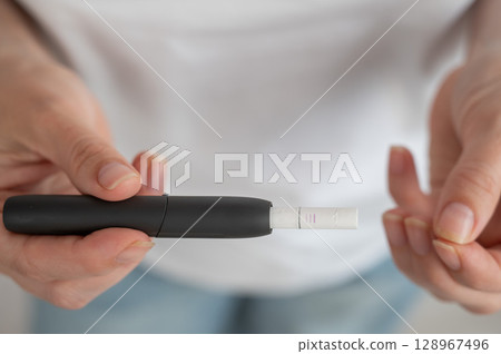 A woman inserts a cigarette stick into a tobacco heating system. Electronic cigarette. A woman inserts a cigarette stick into a tobacco heating system. Electronic cigarette. 128967496