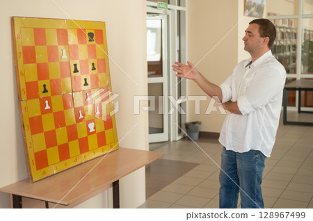 Caucasian man standing at wall mounted magnetic chessboard demonstration.  128967499