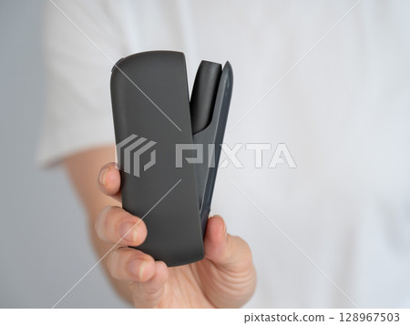 A woman takes a tobacco heating system out of a charger. Electronic cigarette. 128967503