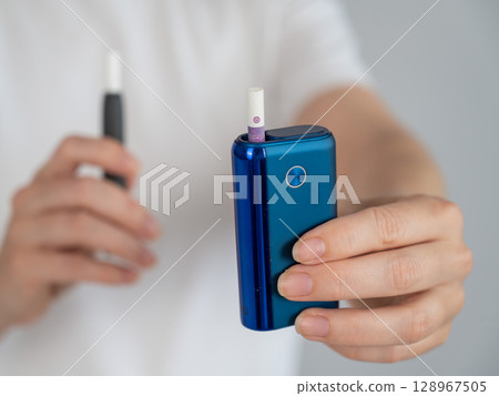 A woman compares two different tobacco heating systems. Electronic cigarette. A woman compares two different tobacco heating systems. Electronic cigarette. 128967505