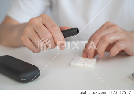 A woman inserts a cigarette stick into a tobacco heating system. Electronic cigarette. A woman inserts a cigarette stick into a tobacco heating system. Electronic cigarette. 128967507