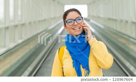 Happy woman stands on a travelator and talks on a cell phone 128967604