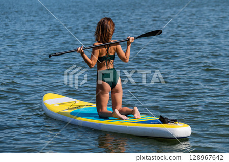 Caucasian woman posing on a SUP board. Summer sport. 128967642