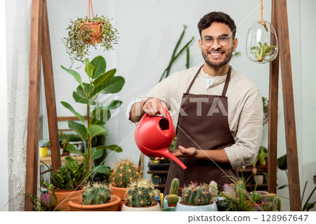 Flower shop assistant watering cactuses and looking contented Flower shop assistant watering cactuses and looking contented 128967647