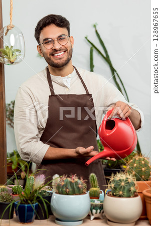 Flower shop assistant watering cactuses and looking contented Flower shop assistant watering cactuses and looking contented 128967655