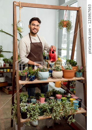 Flower shop assistant watering cactuses and looking contented 128967663