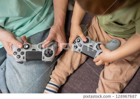 Caucasian woman teaches her little son to play console. Joystick in hands.  128967687
