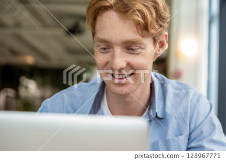 Young smiling man sitting at the table in a cafe and having a video call Young smiling man sitting at the table in a cafe and having a video call 128967771