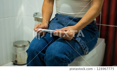 A woman takes an express pregnancy test while sitting on the toilet. A woman takes an express pregnancy test while sitting on the toilet. 128967775
