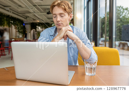 Young smiling man sitting at the table in a cafe and having a video call 128967776