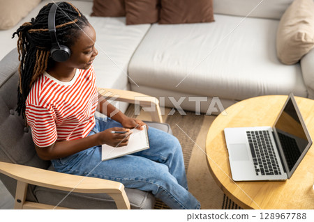 Smiling and contented young african american woman listening something online Smiling and contented young african american woman listening something online 128967788