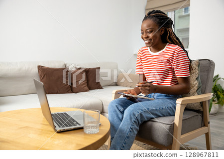 Smiling african american young woman sitting at the laptop and having a video call 128967811