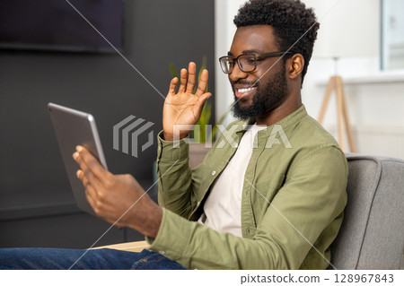 Smiling young african american man having a video call and waving his hand Smiling young african american man having a video call and waving his hand 128967843