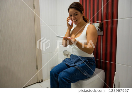 Woman takes express pregnancy test while sitting on toilet and calls husband with smile. Woman takes express pregnancy test while sitting on toilet and calls husband with smile. 128967967