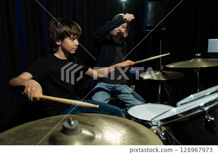 Young caucasian woman teaches a boy to play the drums in the studio on a black background. Music school student 128967973