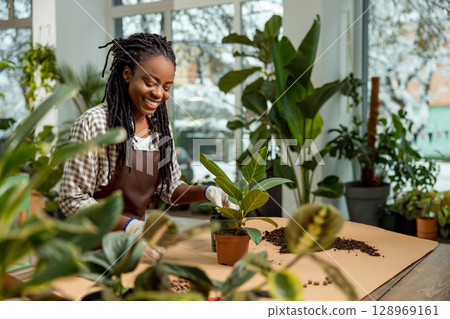 Smiling young woman with dreadlocks plating flowers and looking involved Smiling young woman with dreadlocks plating flowers and looking involved 128969161