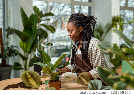 Smiling young woman with dreadlocks plating flowers and looking involved 128969163