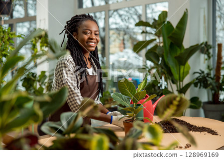 Smiling young woman with dreadlocks plating flowers and looking involved 128969169