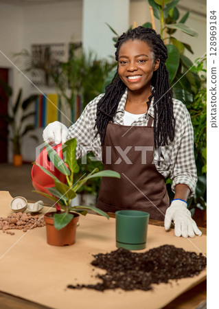 Smiling african american florist planting flowers and looking happy Smiling african american florist planting flowers and looking happy 128969184
