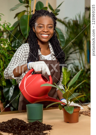 Smiling african american florist planting flowers and looking happy Smiling african american florist planting flowers and looking happy 128969185