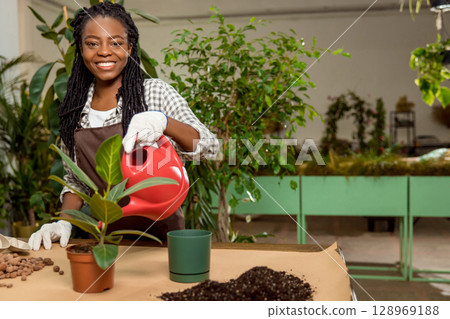 Smiling african american florist planting flowers and looking happy Smiling african american florist planting flowers and looking happy 128969188