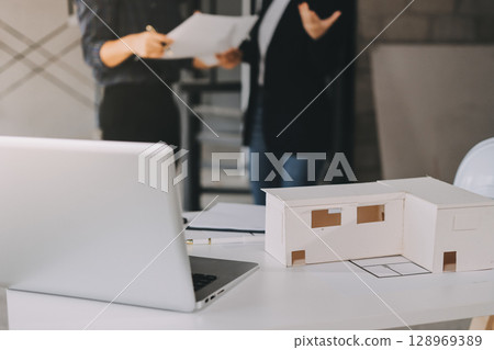 Construction manager and engineer dressed in orange work vests and hard helmets explore construction documentation on the building site near the steel frames 128969389
